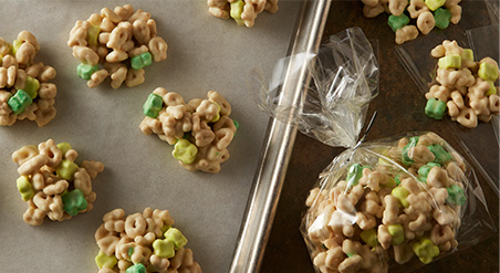 Recipe image of Lucky Charms Leprechaun Nuggets including cereal and mini marshmallows. Servings shown on tray and in clear bag.