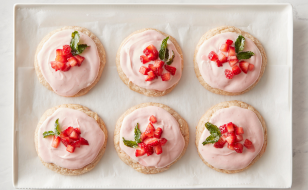 Six round frosted cookies topped with chopped strawberries