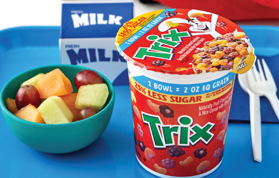 A bowl of cereal, fresh fruit, and a carton of milk on a blue tray, with a Trix yogurt cup in the foreground.