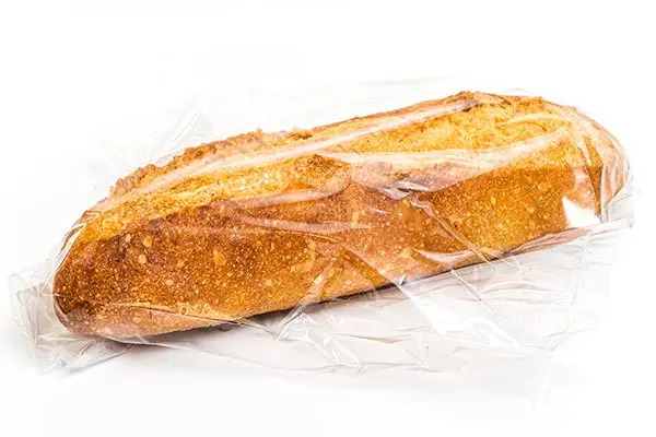 A baguette wrapped in clear plastic resting on a plain white background.