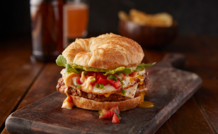 Croissant sandwich with chorizo sausage, cheese and lettuce sitting on wooden serving tray.